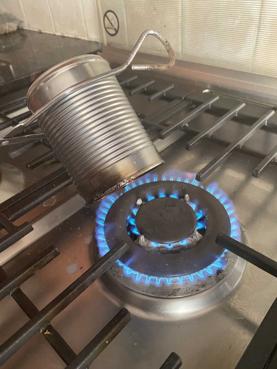 A can held by tongs over an open gas flame